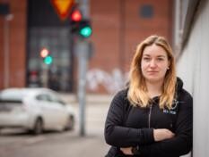 En kvinna lutar mot väggen. I bakgrunden syns trafikljus och en bil.